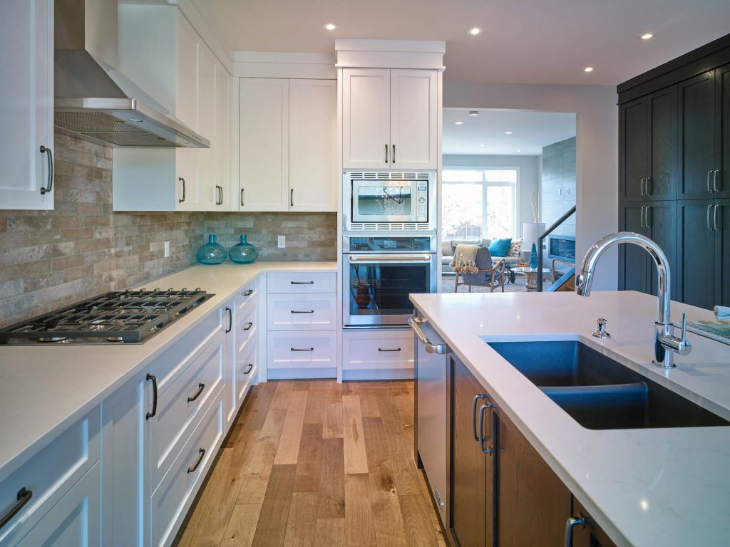 Open and bright modern farmhouse kitchen with full-height white cabinets and counters, hardwood flooring and state-of-the-art built-in appliances.