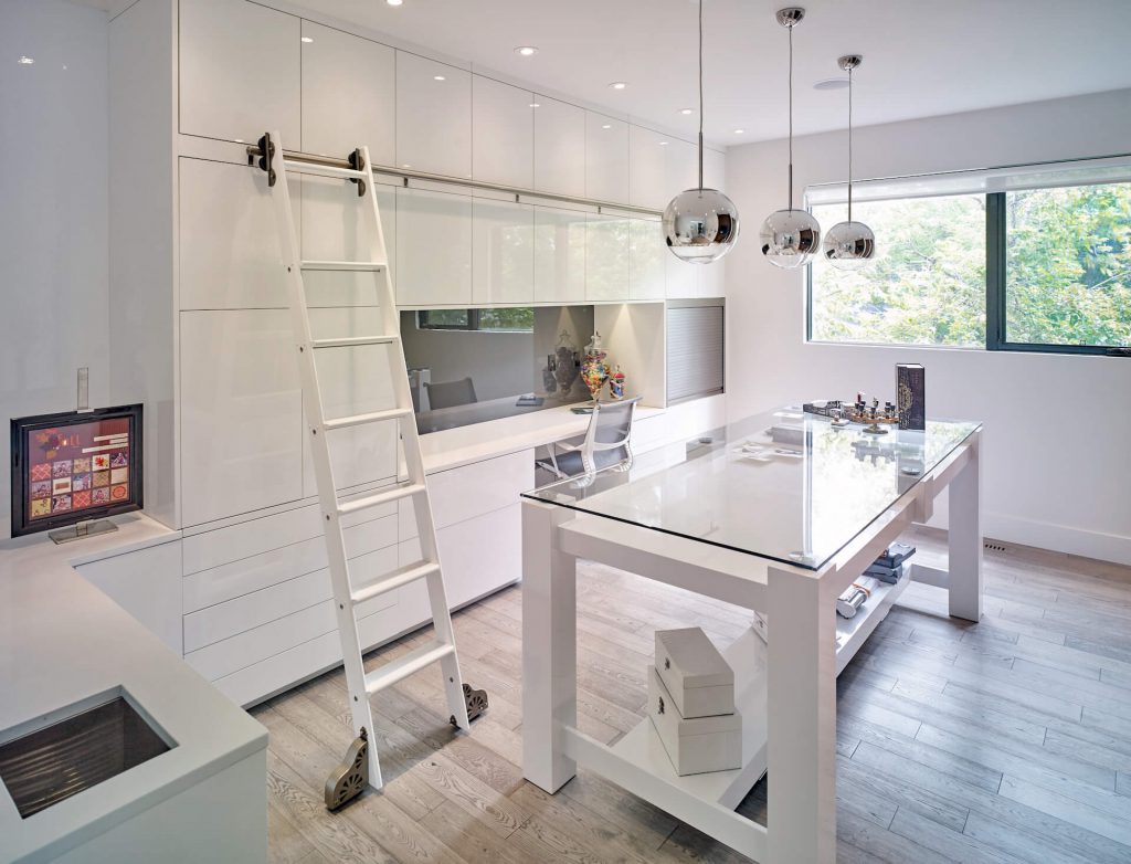Sleek, minimal flex room with white floor-to-ceiling cabinets, built-in desk, rolling ladder and glass rectangular table